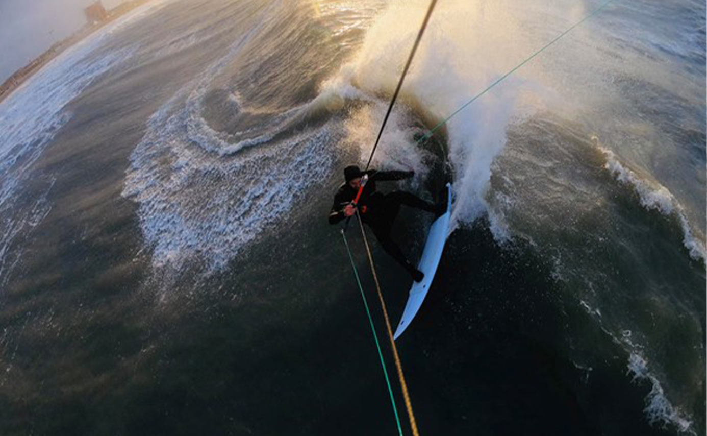 Kitesurfer fährt tief in einer tubenden Welle, die Kiteleinen straff gespannt