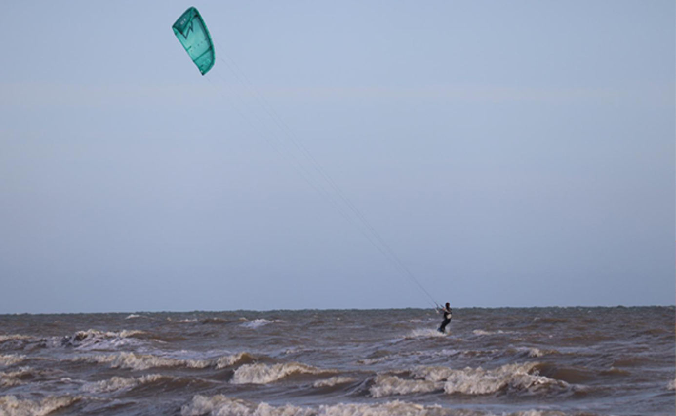 Einzelner Kitesurfer weit draußen auf kabbeliger grauer See, kleiner türkiser Kite hoch am Himmel